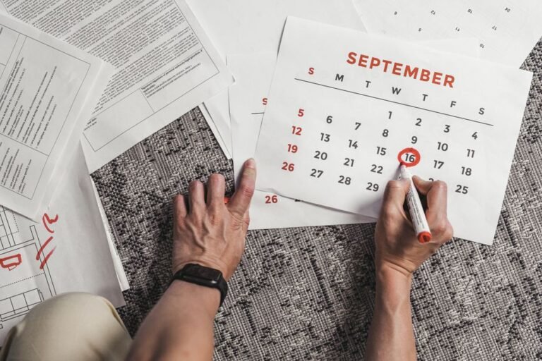 An adult sitting at a table looking at a wall calendar with one date circled