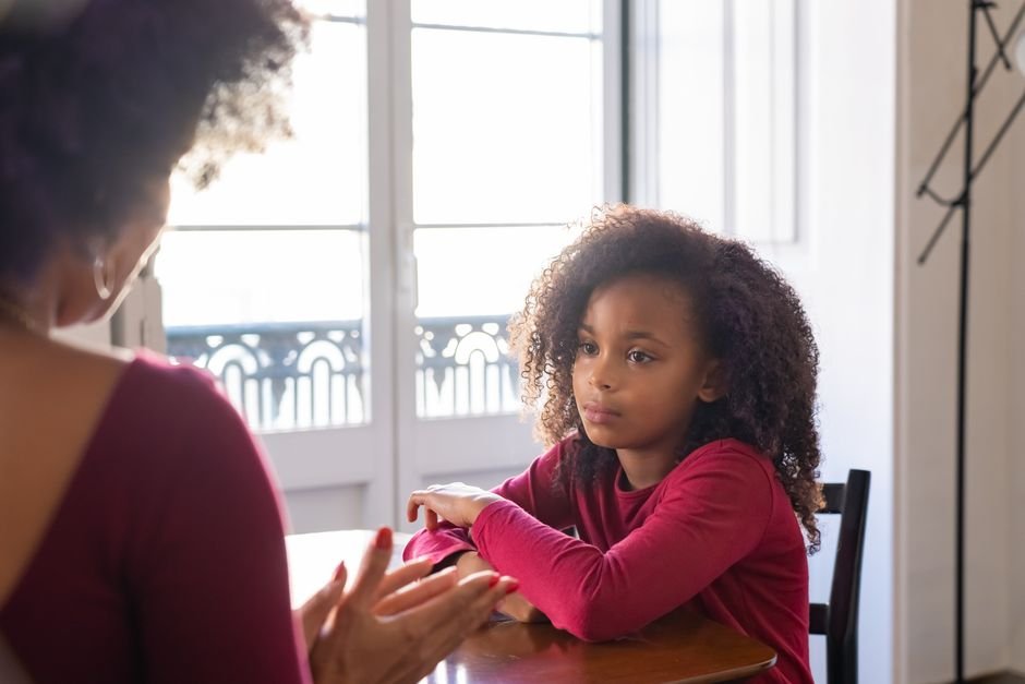 A child and adult sitting at a table, mid-conversation, looking at each other