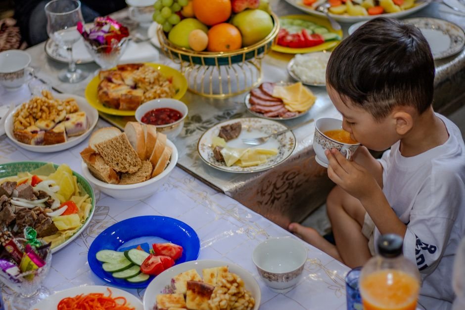 A child sitting at a kitchen table with a plate of separated foods, including crackers, apple slices, and pasta.
