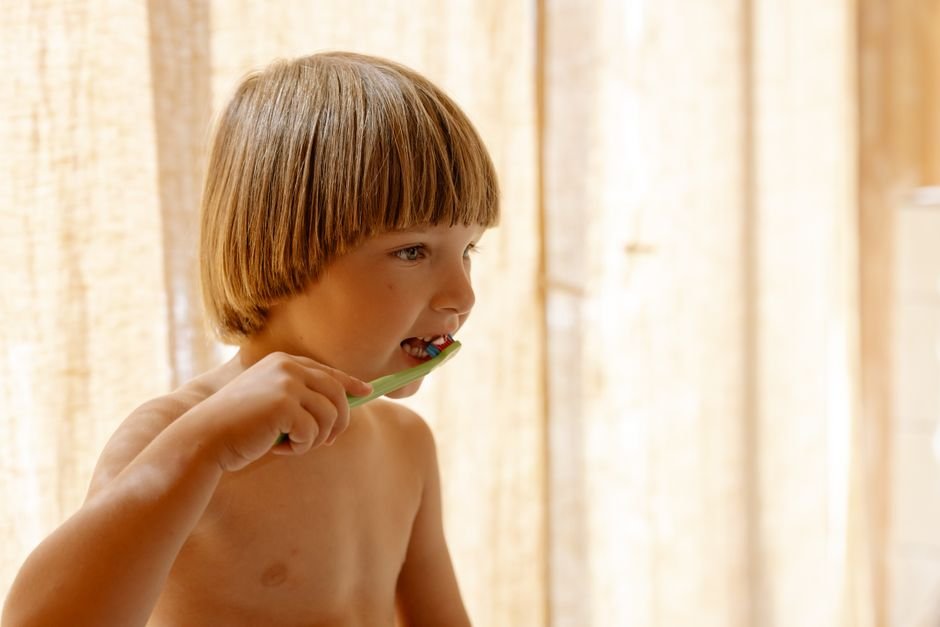 What Makes Toothbrushing Genuinely Easier for a Sensory-Sensitive Child A young child standing at a bathroom sink holding a toothbrush, with a parent beside them
