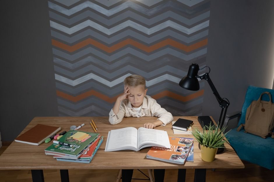What Makes Homework Genuinely Manageable for an Autistic Student A child sits at a tidy desk writing in a notebook, with a pencil cup and a lamp beside them.