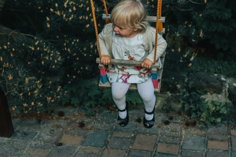 A child sitting on a playground swing, moving gently, with trees in the background
