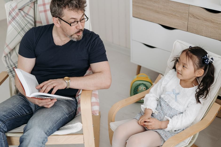A child sitting in a clinic chair holding a parent's hand while a nurse prepares a tray nearby.