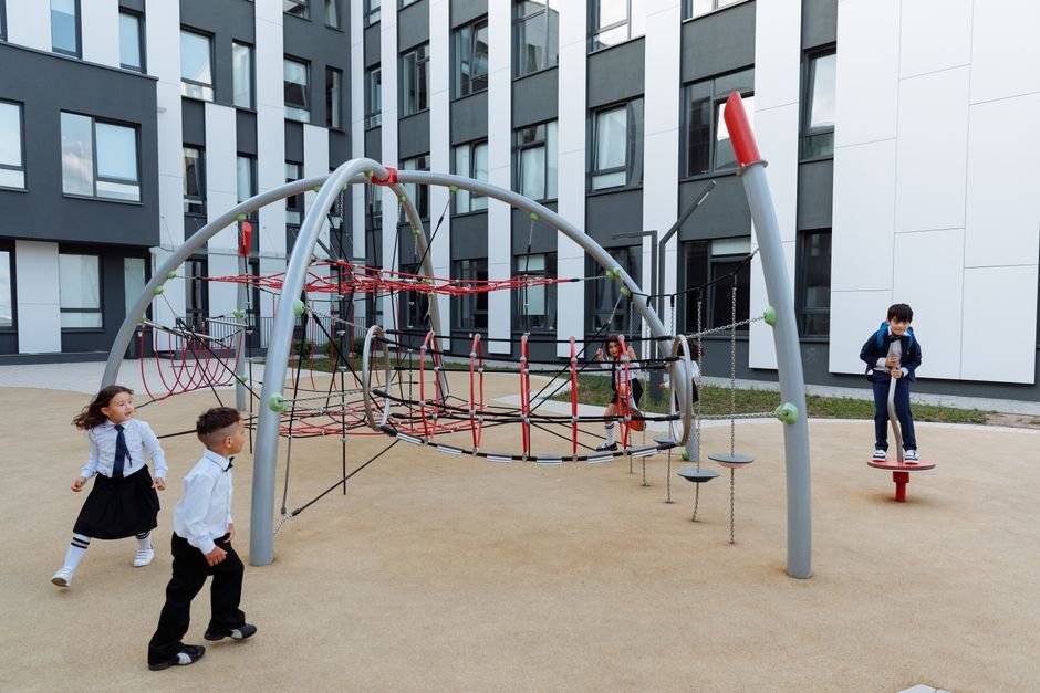 Common Mistakes Schools Make With Unstructured Time Like Recess Children play on a school playground, some on a climbing frame and others sitting on a bench nearby.