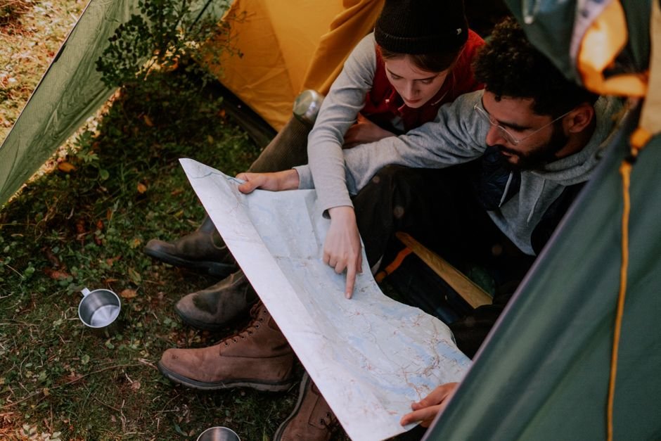 A parent and child sitting together at a table, looking over a printed trip itinerary and a map.