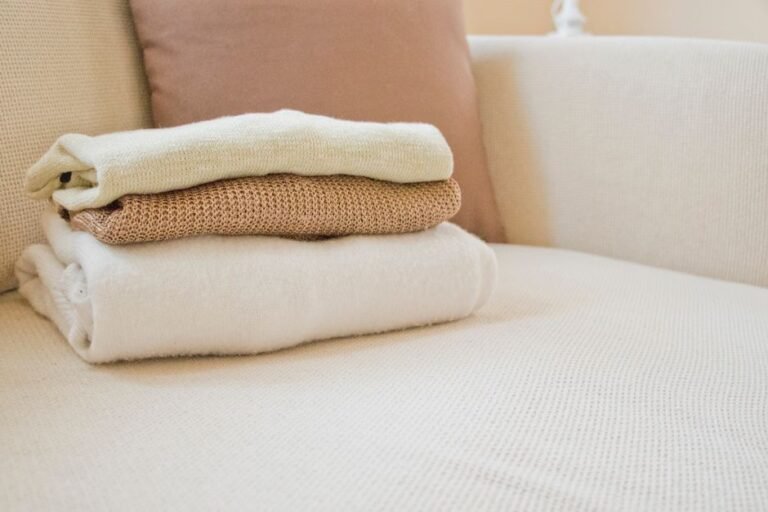 A thick knitted blanket folded over the arm of a sofa in a softly lit living room.