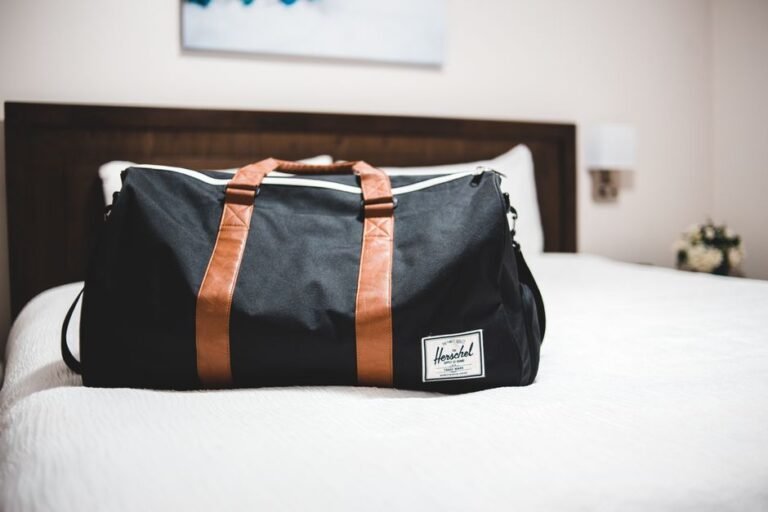 An open overnight bag on a bed holding folded pajamas, headphones, a soft toy and a small notebook.