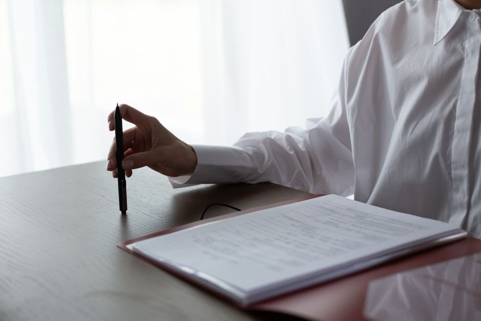 A parent sits at a kitchen table with a printed document, a highlighter, and a mug of tea.