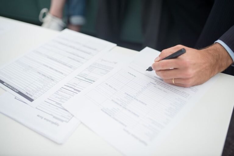 A parent hands a folder of papers across the front desk of a school office to a staff member.