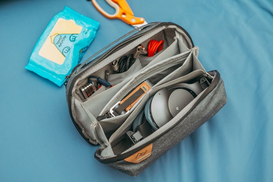 A small packed bag with noise-cancelling headphones, sunglasses, and a fidget toy laid beside it
