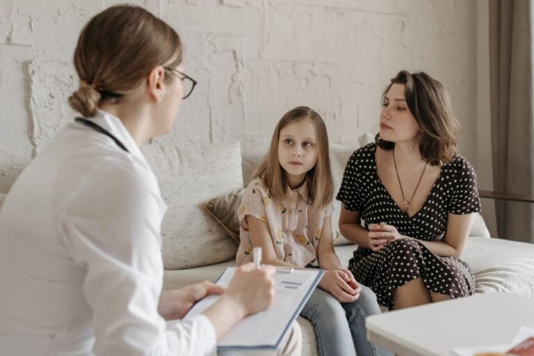 A teenager sitting across a desk from a doctor while a parent sits a little to one side, listening.