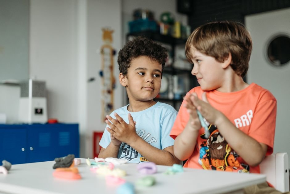 Two young children sitting near each other on a rug, each absorbed in a separate toy