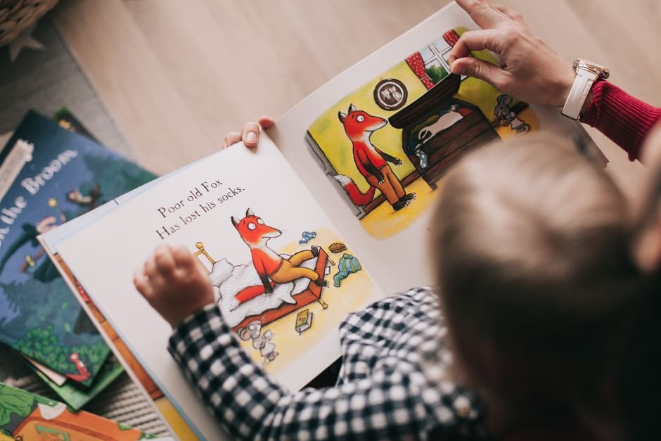 A child sitting cross-legged on a rug, reading a picture book